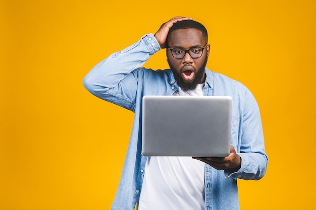 Young surprised african man standing and using laptop computer