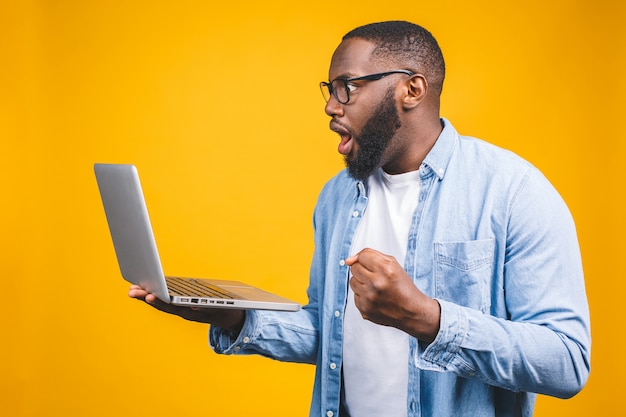 Young surprised african man standing and using laptop computer