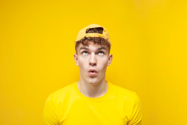 黄色い帽子とTシャツを着た若い驚いた男が見上げる