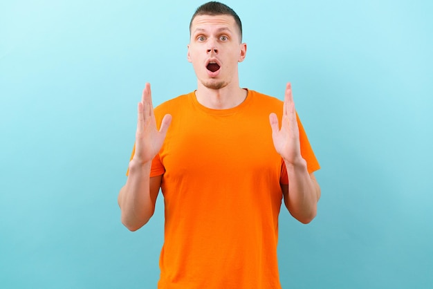 Молодой удивленный мужчина с открытым ртом, показывающий обеими руками знак большого размера на синем фоне