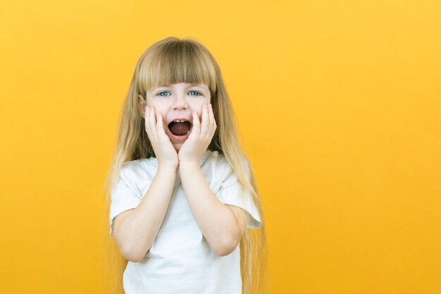 Giovane sorpresa scioccata pazza bambina sorridente che tiene le mani isolate su sfondo giallo