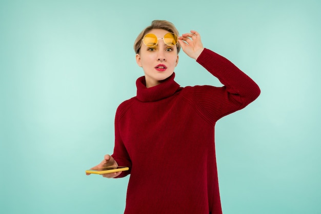 A young surprised woman in a red sweater with a smartphone on a blue background