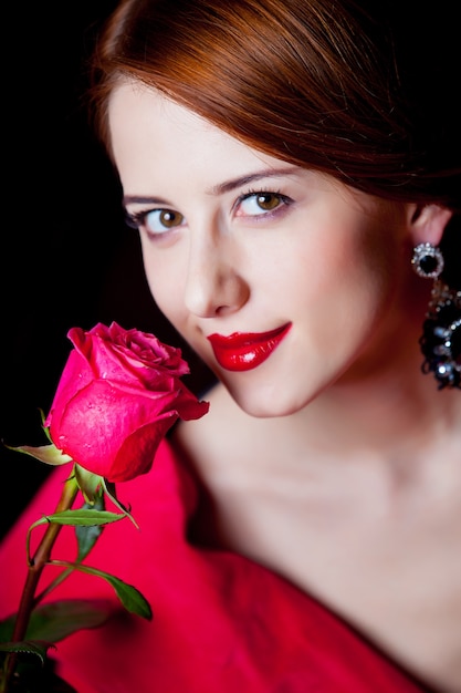 Young surprised woman in red Victorian epoch clothes with red rose on dark