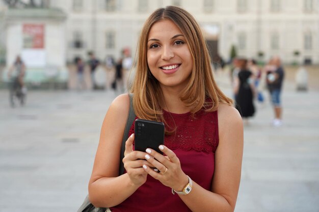 長い髪の若い甘い女性が携帯電話を持ってカメラを見る