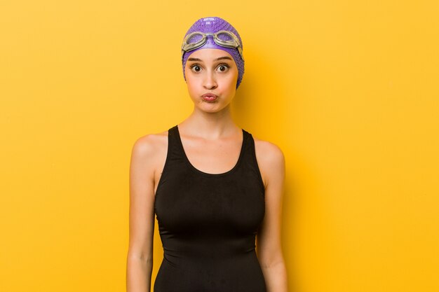 Young swimmer caucasian woman blows cheeks, has tired expression.