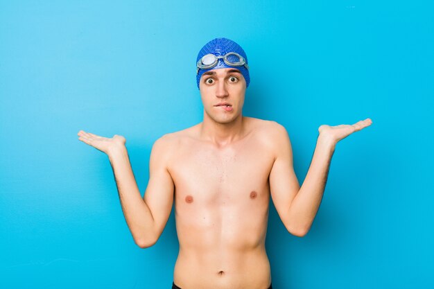 Young swimmer man confused and doubtful shrugging shoulders to hold a copy space.