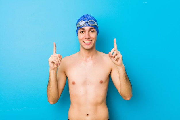 Young swimmer man indicates with both fore fingers up showing a blank space.