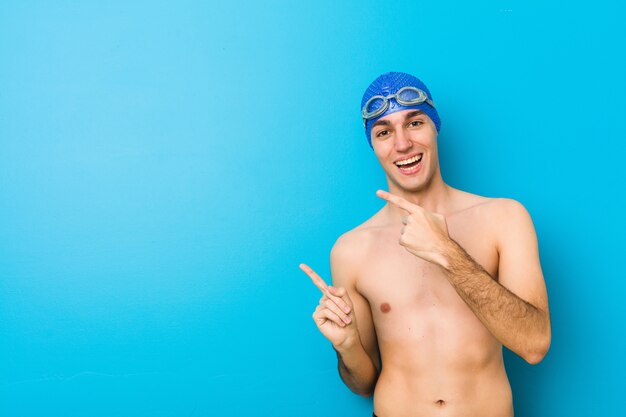 Young swimmer man pointing with forefingers to a copy space, expressing excitement and desire.