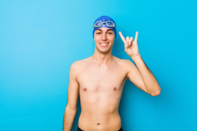 Young swimmer man showing a horns gesture as a revolution concept.