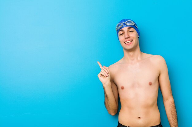 Young swimmer man smiling cheerfully pointing with forefinger away.