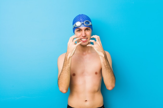Young swimmer man upset screaming with tense hands.