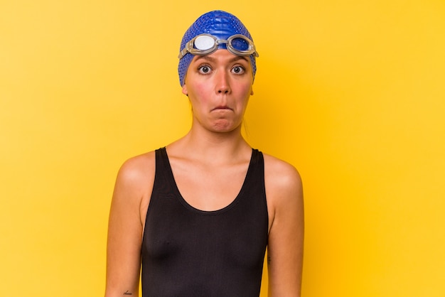 Young swimmer venezuelan woman isolated on yellow background\
shrugs shoulders and open eyes confused.