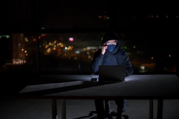 Photo young talented hacker using laptop computer while working in dark office with big city lights in the background at night