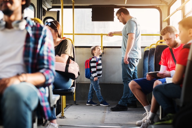 젊은 키가 큰 아버지와 그의 작은 아들은 버스의 뒤쪽 끝에 서서 서로를보고 있습니다.