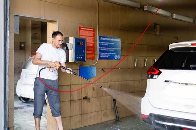 Giovane uomo alto che schizza la sua auto con un tubo da giardino