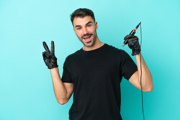 Young tattoo artist man isolated on blue background smiling and showing victory sign