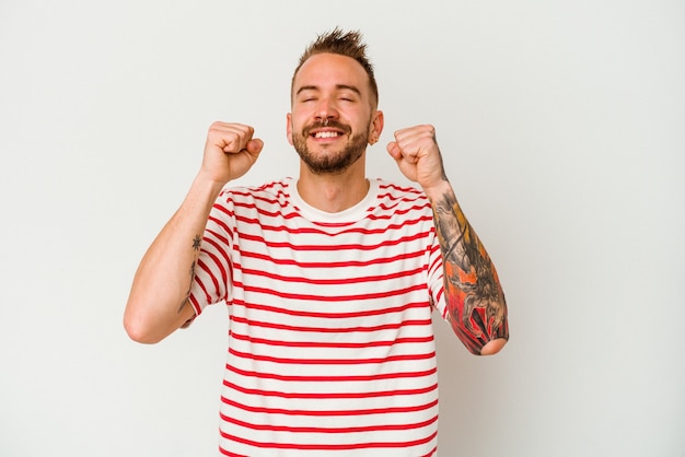 Young tattooed caucasian man isolated on white background celebrating a victory, passion and enthusiasm, happy expression.