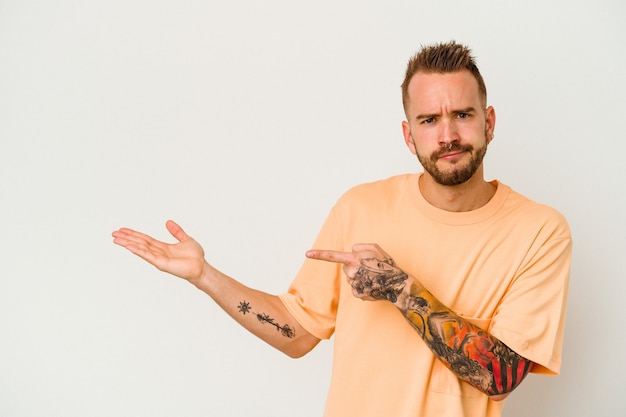 Young tattooed caucasian man isolated on white background excited holding a copy space on palm.