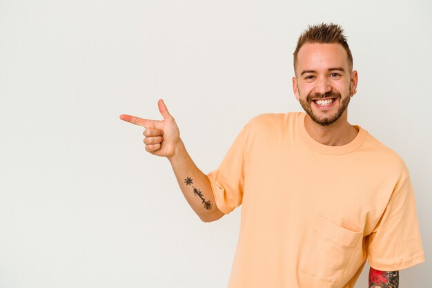 Young tattooed caucasian man isolated on white background smiling cheerfully pointing with forefinger away.