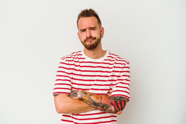 Young tattooed caucasian man isolated on white background unhappy looking in camera with sarcastic expression.