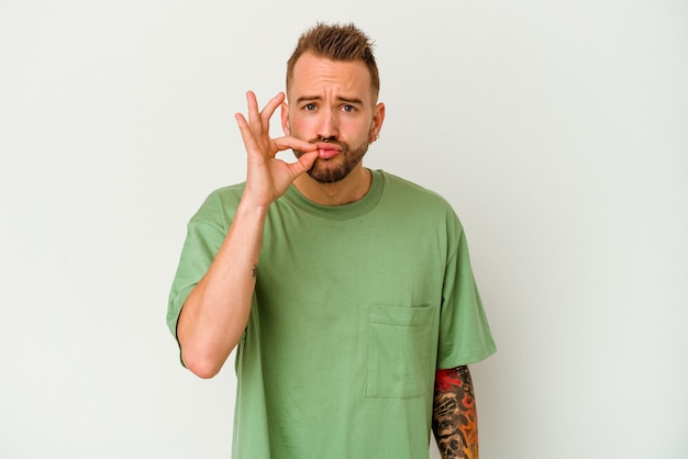 Young tattooed caucasian man isolated on white background with fingers on lips keeping a secret.