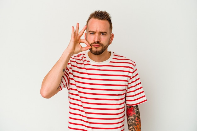 Young tattooed caucasian man isolated on white background with fingers on lips keeping a secret.