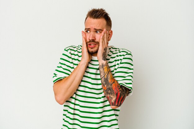 Young tattooed caucasian man isolated on white wall scared and afraid.