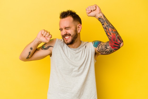 Young tattooed caucasian man isolated on yellow background celebrating a special day, jumps and raise arms with energy.