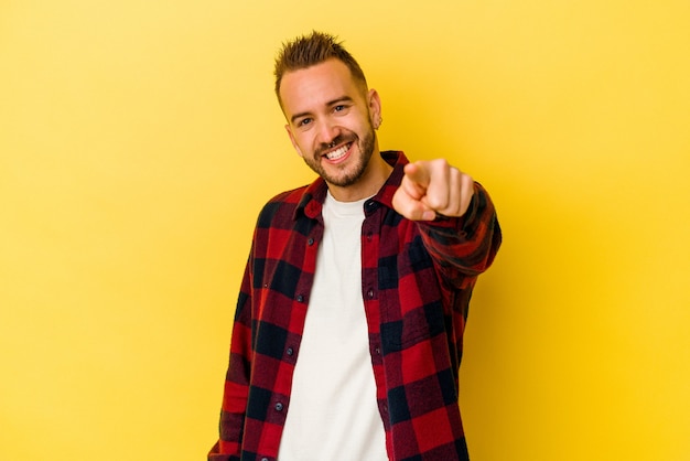Young tattooed caucasian man isolated on yellow background cheerful smiles pointing to front.