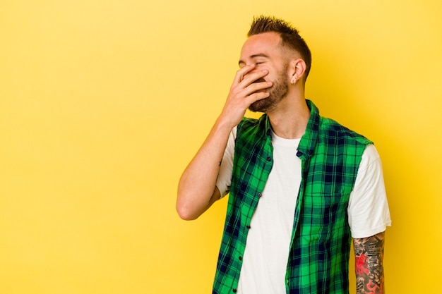 Young tattooed caucasian man isolated on yellow background laughing happy, carefree, natural emotion.