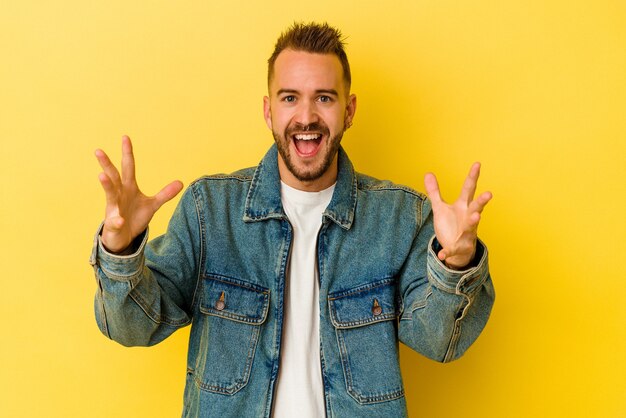 Young tattooed caucasian man isolated on yellow background receiving a pleasant surprise, excited and raising hands.