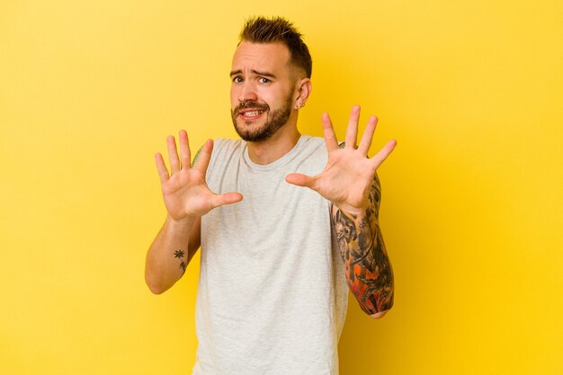 Young tattooed caucasian man isolated on yellow background rejecting someone showing a gesture of disgust