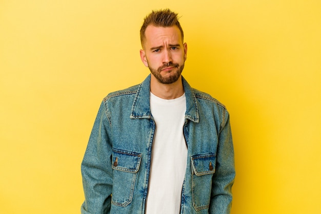 Photo young tattooed caucasian man isolated on yellow background sad, serious face, feeling miserable and displeased.