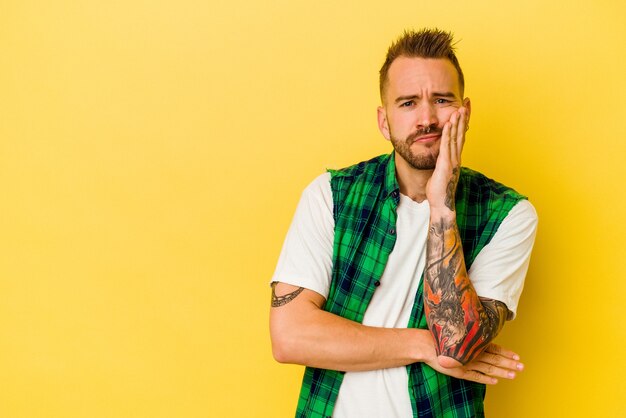 Young tattooed caucasian man isolated on yellow wall who feels sad and pensive, looking at copy space.