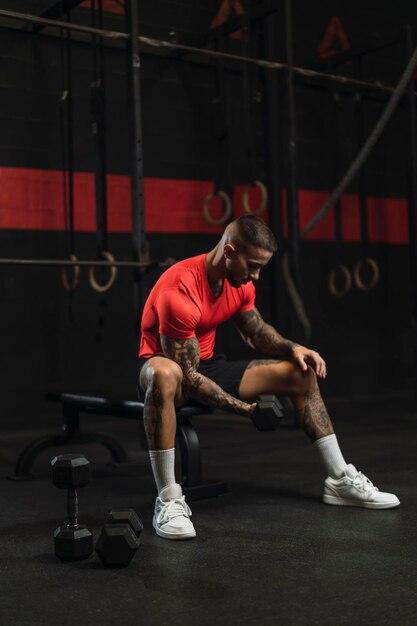 young tattooed guy doing sports in a gym with a red shirt