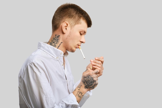 Young tattooed man lights a cigarette in the studio