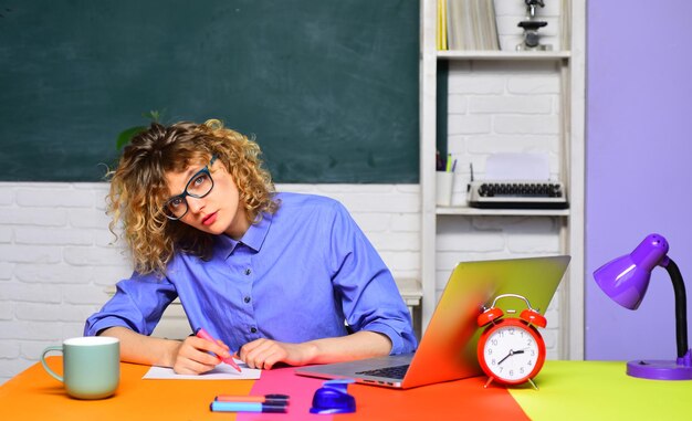 Young teacher in glasses over green chalkboard background female university student sits on desk