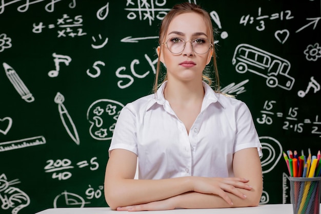 Young teacher is sitting near blackboard in classroom