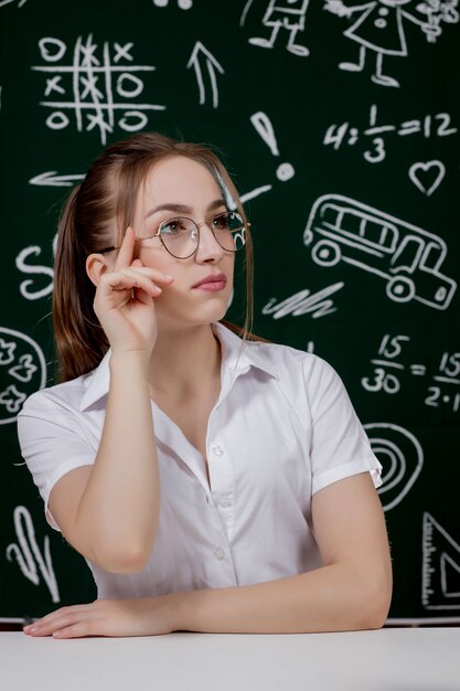 Young teacher is sitting near blackboard in classroom