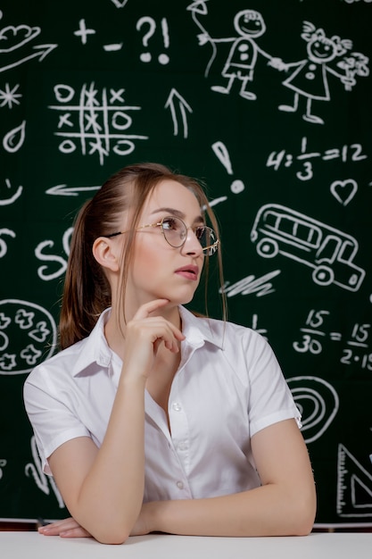 Young teacher is sitting near blackboard in classroom