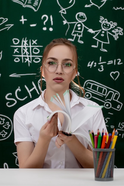 Young teacher is sitting near blackboard in classroom