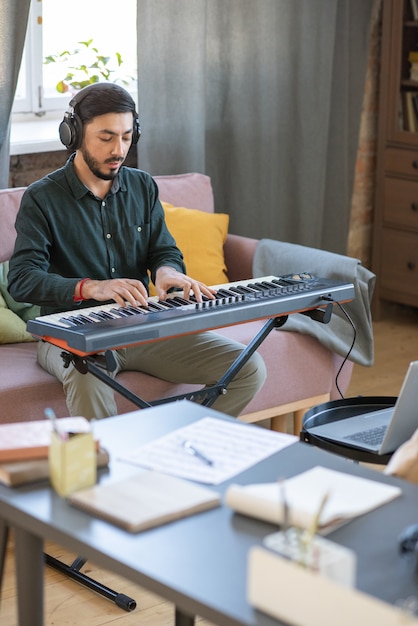 Giovane insegnante di musica che suona la tastiera del pianoforte davanti al laptop