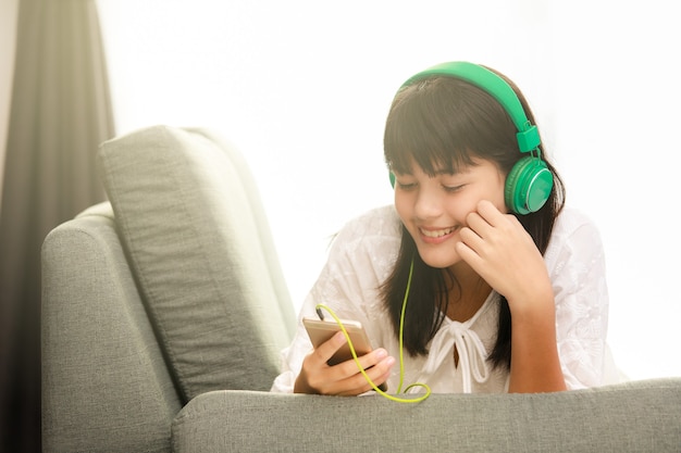 Young teen Asian girl listening to music with headphone and smarthphone at home with happiness manner