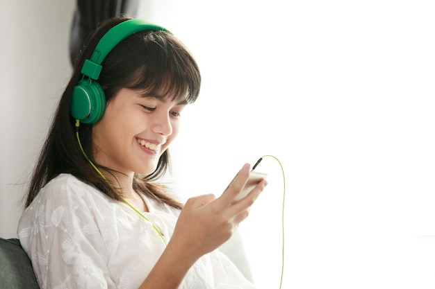 Young teen Asian girl listening to music with headphone and smarthphone at home with happiness manner