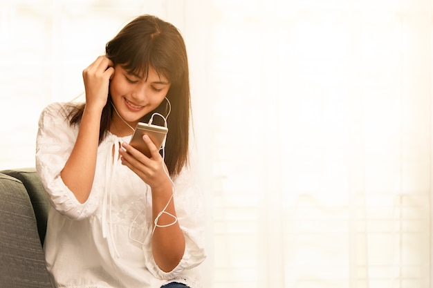 Giovane ragazza asiatica adolescente che ascolta musica con cuffie e smartphone a casa con modi felici