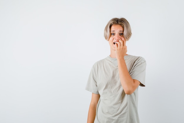 Young teen boy biting nails emotionally in t-shirt and looking troubled. front view.