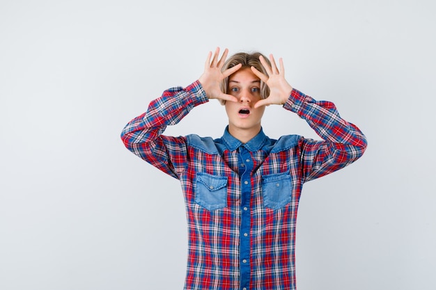 Young teen boy in checked shirt peeking through fingers and looking wondered