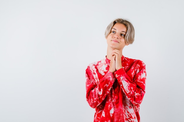 Young teen boy clasping hands in praying gesture, looking away in shirt and looking dreamy. front view.