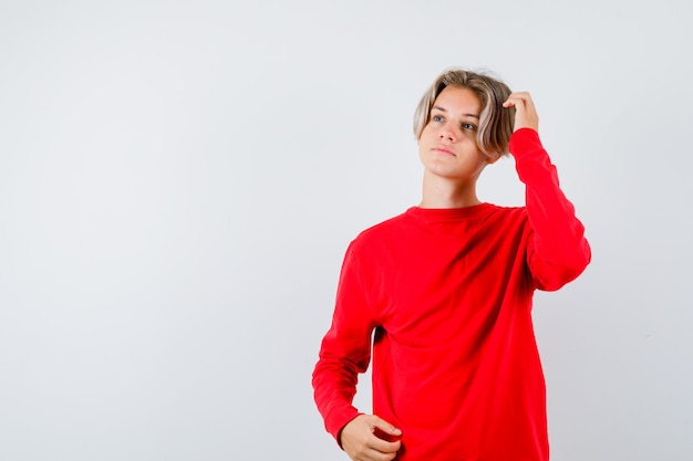 Young teen boy looking away while scratching head in red sweater and looking pensive. front view.