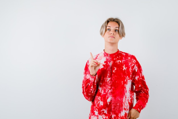 Young teen boy pointing up, looking upward in shirt and looking focused , front view.